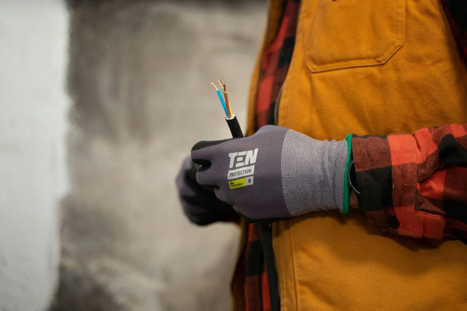A tradesperson in work gloves holding a stripped electrical cable