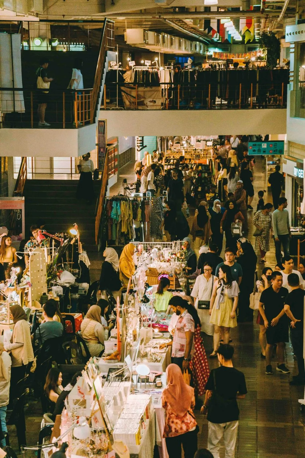 Shoppers browsing clothing and handmade stalls at an indoor weekend market